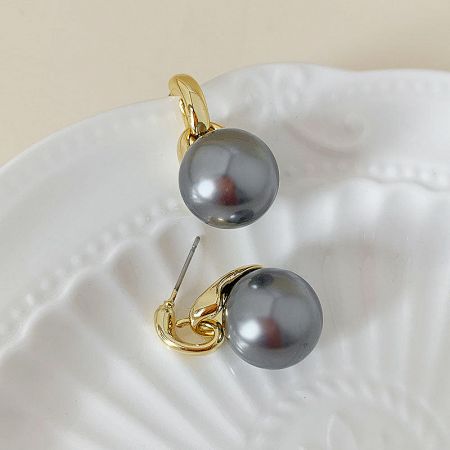 Stylish dark gray pearl earrings with gold settings displayed on a shell dish.