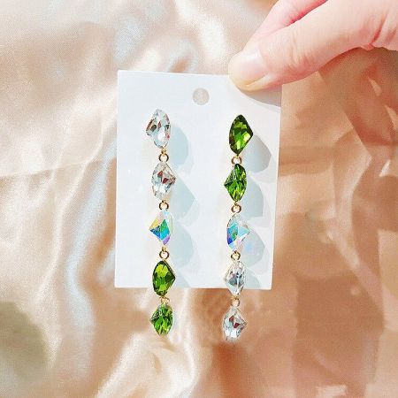 Detailed shot of the teardrop-shaped green and clear gemstones on the gold-plated dangle earrings.