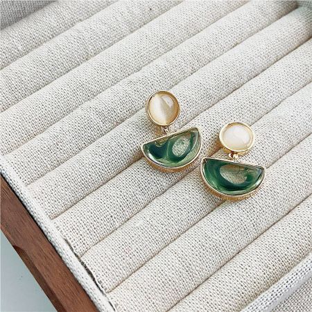 Close-up of gold earrings with green and white stone accents.