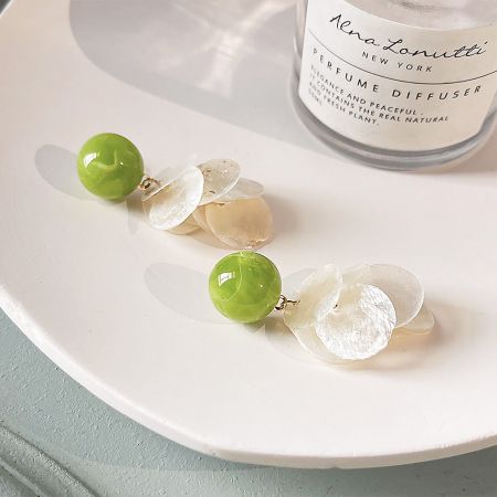 Product shot of the green bead and shell earrings with an Alena Lonutti perfume diffuser for scale and style.