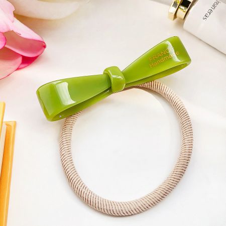 A single vibrant green acetate bow hair tie with a beige elastic band.