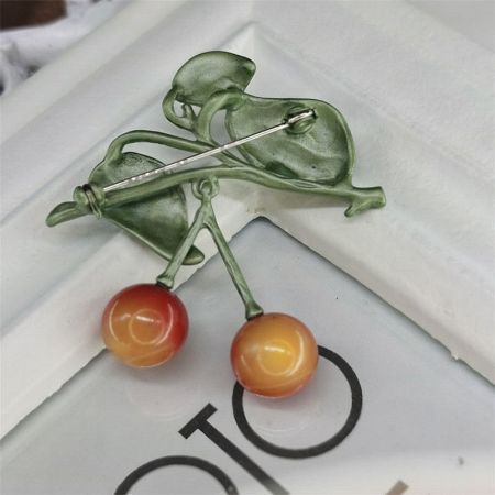 Detailed view of the cherry brooch highlighting the green leaf and stem detail.