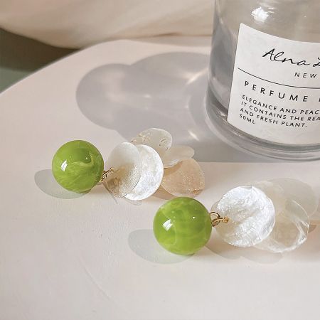 Lifestyle shot of the green and white shell earrings styled next to a perfume bottle.