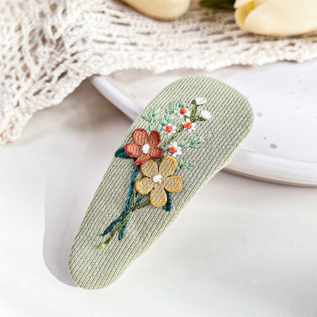 Detailed shot of the green fabric hair clip with delicate floral embroidery.
