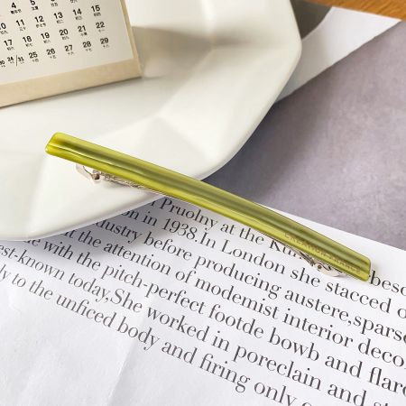 A stylish green acetate hair clip resting on an open book.