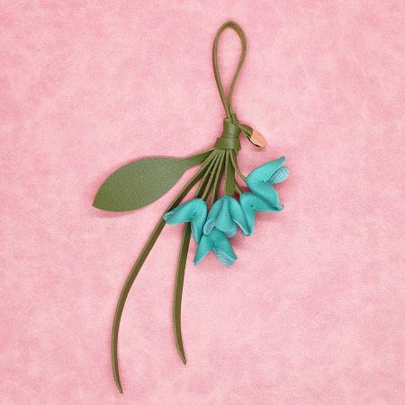 Teal blue PU leather flower bag charm with a green leather strap, shown against a pink background.