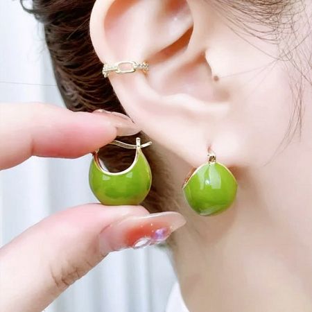 A close-up view of the green spherical earring being worn, highlighting its glossy finish.