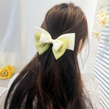 A large, stylish ribbon bow hair clip worn in long brown hair.