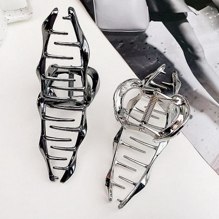 A close-up of two metal hair clamp clips, one in a matte black finish and the other in a polished silver finish.