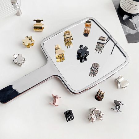 Various mini metal hair clips in gold, silver, and black displayed with their reflections.