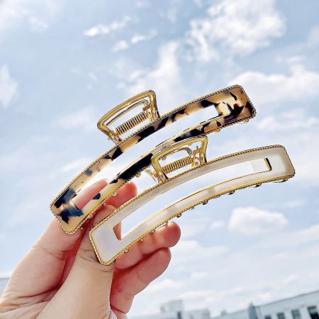 Two elegant hair claws, one in a tortoiseshell pattern and one in white, both with gold metal details.