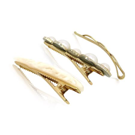 Close-up of two hair clips from the set: one cream-colored and one gold with delicate pearl details.