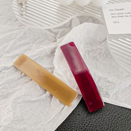 A pair of rectangle hair clips in tan and dark red colors.