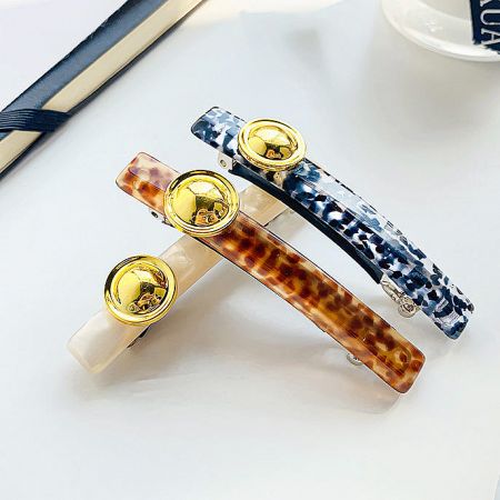 A close-up view of three acetate hair clips featuring sophisticated gold accents.