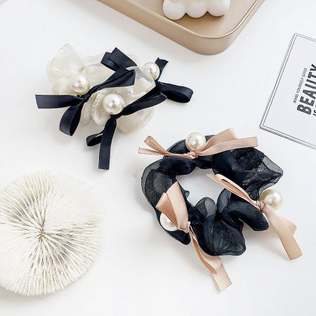 A pair of stylish hair scrunchies, one black and one white, adorned with flowing ribbons and pearls.