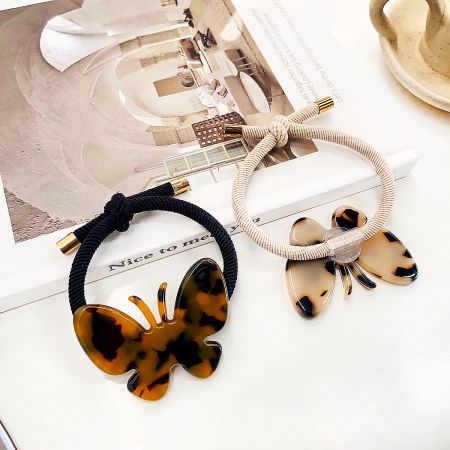 Close-up of two butterfly hair ties, one in a pink marble and the other in a multi-color pattern.