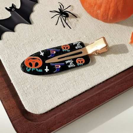 A white no-crease hair clip decorated with orange pumpkins and black witch hats.