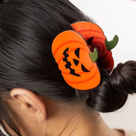 A single pumpkin hair clip held up to display its size and claw mechanism.