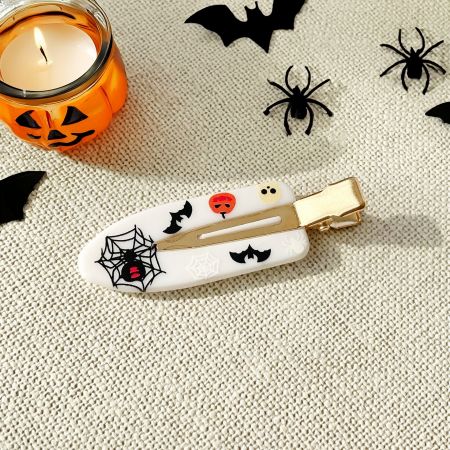 A white no-crease hair clip with a black spiderweb and pumpkin design.