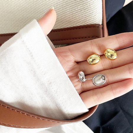 A hand holding multiple pairs of the gold and silver small bean stud earrings to show scale and finish.