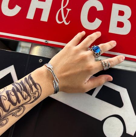 Lifestyle image of the feather bangle worn on a tattooed arm, demonstrating its fashionable appeal.