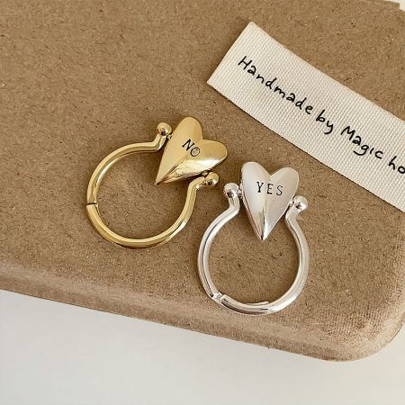 A minimalist silver-plated brass ring with an adjustable band and a heart engraved with 'NO'.
