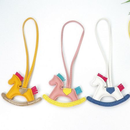 Close-up of three handmade-style leather rocking horse charms in yellow, pink, and white.