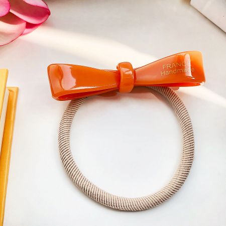 A bright orange handmade acetate bow hair tie, perfect for a pop of color.