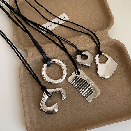 Assortment of minimalist brass pendants including comb, heart, and round shapes.