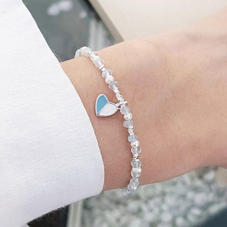Close-up of a sterling silver bracelet with a blue enamel heart charm and white pearl beads.