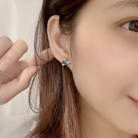 A model wearing a heart-shaped silver huggie earring with a central blue gemstone, demonstrating its elegant fit.