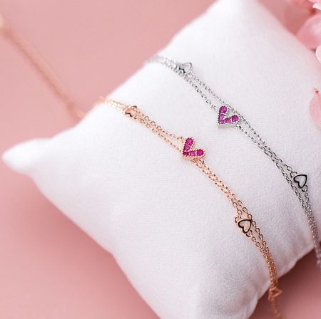 Close-up view of two heart-shaped bracelets, one rose gold and one silver, featuring pink gemstone hearts.