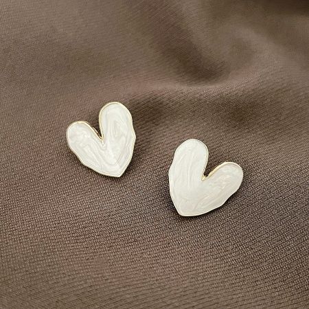 Close-up of the white enamel heart earrings with a marbled pattern and gold border on a textured surface.