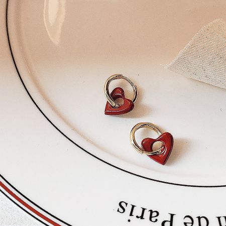 Close-up of the red and gold heart-shaped earrings on a white display plate.