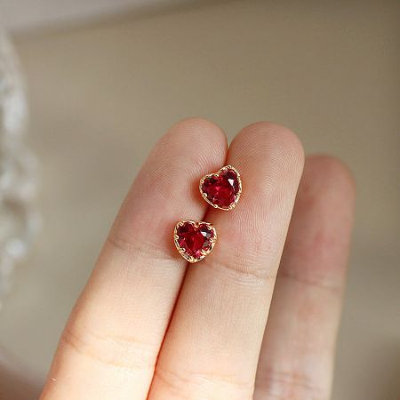 925 Sterling Silver Gold Red Heart Stud Earrings (5 Pairs) - A close-up of delicate 925 sterling silver stud earrings, featuring a gold-plated red heart design, held between fingers to show scale.