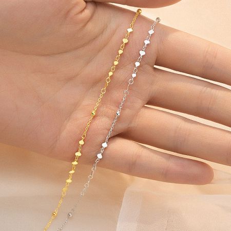 A hand holding both the gold and silver heart link bracelets.
