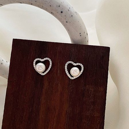 Detailed view of the heart-shaped pearl earrings, highlighting the silver craftsmanship and central pearl.