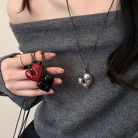 Model showcasing chunky heart pendant necklaces in red, black, and silver.