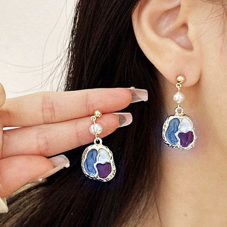 Stylish earrings featuring heart-shaped stones in blue, purple, and white, set in gold with a pearl.
