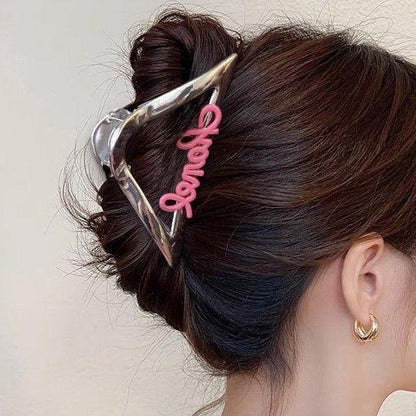 Close-up of a silver hair clip with pink 'Honey' lettering securing a dark hair bun.