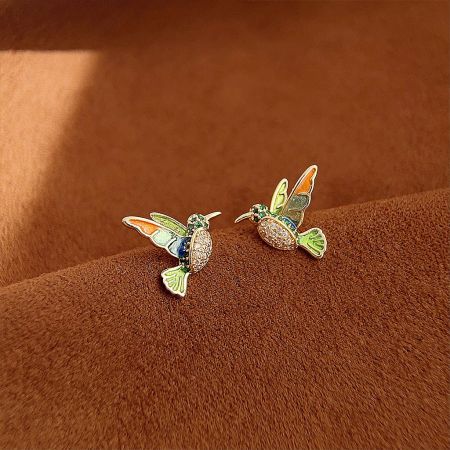 Detailed shot of a pair of gold-plated hummingbird stud earrings with vibrant enamel and sparkling stones.