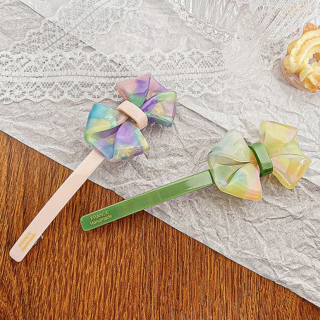 Two iridescent bow hair clips, one pink and one multi-colored, highlighting the shiny finish.
