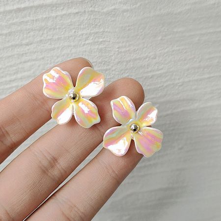 A hand holding the iridescent flower earrings to display their size and finish.