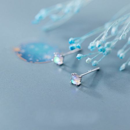 A pair of silver moonstone stud earrings on a decorative blue background.