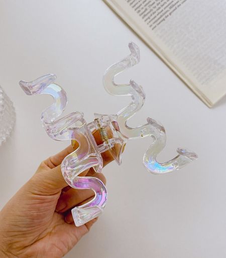 Close-up of a single iridescent acrylic hair clip with a unique spiral design, showcasing its rainbow colors.