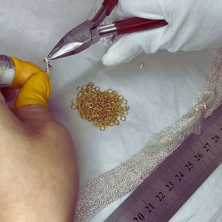 Close-up of an expert jeweler connecting links of a delicate chain, a key step in jewelry assembly.