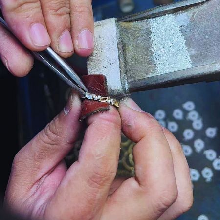 Close-up of a craftsman setting diamonds onto a gold chain.