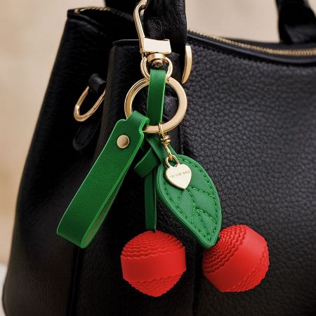 Wholesale Cherry Keychain Cute Bag Charm PU Leather Purse Keychain Bulk (5 pcs) - A stylish red PU leather cherry keychain with a green leaf charm attached to the handle of a classic black handbag, showcasing its use as a cute bag accessory.