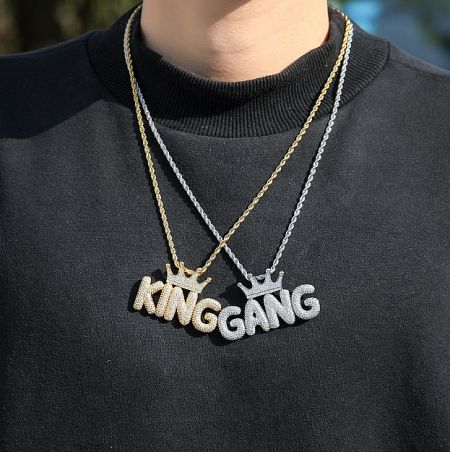 Gold and silver 'KINGGANG' necklaces with crown pendants worn on a black sweater.