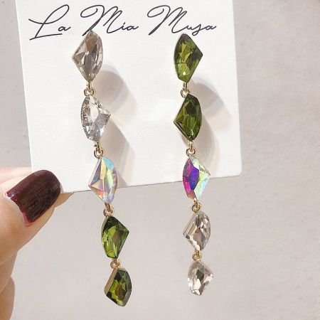 Close-up view of the long rhinestone dangle drop earrings with clear and green gemstones on a display card.